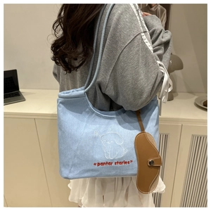 Detail of light blue denim tote bag with cute puppy embroidery and brown leather charm