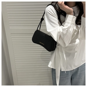 Detail of black woven shoulder bag featuring golden lettering and adjustable knotted strap