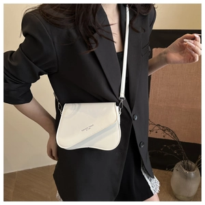 Detail of cream leather crossbody bag with wave flap design on black suit