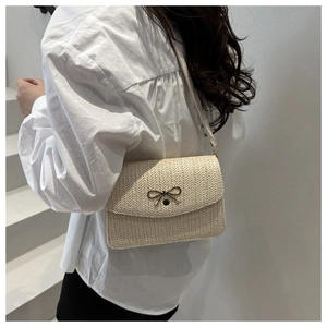 Detail view of beige woven handbag with golden bow buckle on a white background