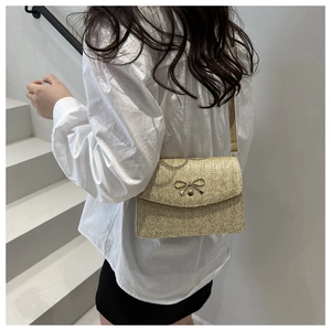 Detail of beige woven crossbody bag with a golden bow-shaped clasp for women