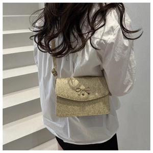 Detail view of woven beige crossbody bag with a gold metal bow and adjustable strap