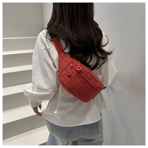 Détail d'un sac bandoulière en tweed rouge à double zip porté sur un escalier blanc