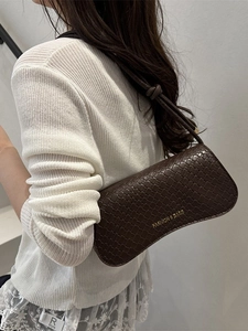 Brown woven texture baguette bag with shoulder strap and gold lettering shown on model