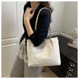Detail of white textured fabric tote bag featuring gold chain and brand logo patch