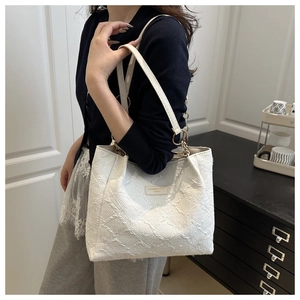 Detailed shot of white jacquard tote bag with leather strap and gold chain on shoulder