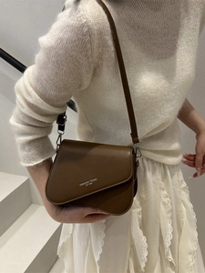 Chic dark brown crossbody bag with wave-edge flap worn with white knit sweater
