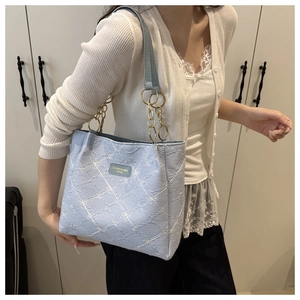 Close-up of light blue tote bag featuring white floral embroidery and gold chain handle
