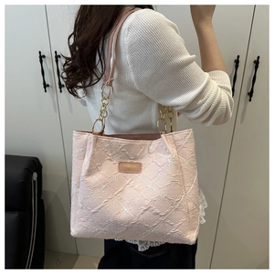 Detail of pink embroidered tote bag with white floral patterns and gold chain strap