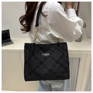 Detail of a black quilted tote bag with sequins and a gold chain strap worn by a model