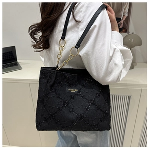 Detail of black knit tote bag showing textured glitter lattice pattern and gold chain strap