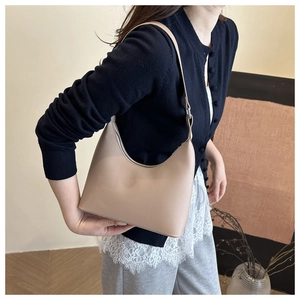 Detailed side view of beige leather crescent shoulder bag worn with casual knitwear