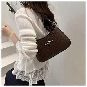 Détail du sac à bandoulière tressé marron foncé avec étoile argentée sur escalier blanc