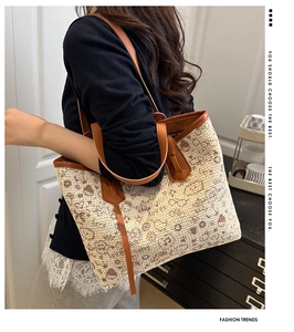 Detail of a large woven tote bag with cartoon patterns and brown leather handle on model