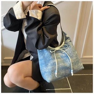 Detail of blue denim hobo bag with white bow knot and beads shown in stylish lifestyle setting