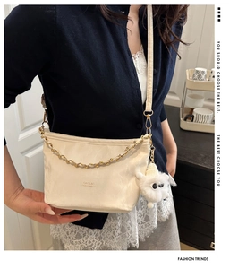 Detail of cream crossbody bag with gold chain, pleated leather, and plush sheep charm