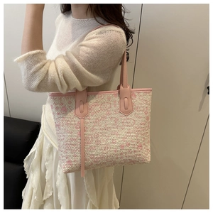 Detail of pink woven straw tote bag with leather straps on a model's shoulder