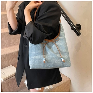 Macro view of light blue denim tote with brown leather bow and beaded tassels detail