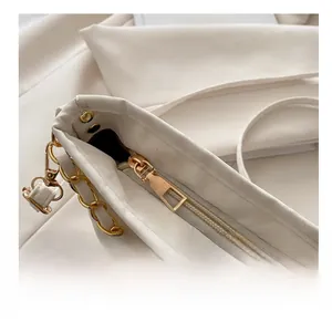 Close-up of smooth gold metal zipper and chunky chain on a white textured bucket bag