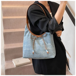 Detail of light blue denim tote bag with leather bow, beads and shoulder strap on model