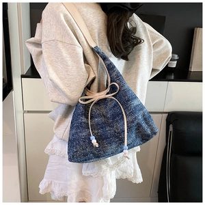 Detail of denim tote bag featuring cream leather strap and decorative bow with beads