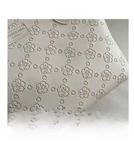 Detailed view of embossed floral patterns and brand logo on cream faux leather tote bag