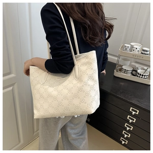 Detail of cream white tote bag featuring intricate floral embossing and metal logo plaque