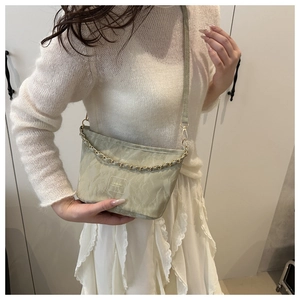 Detail of light green bucket bag with pleated fabric texture and gold chain strap
