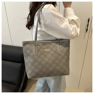 Detail of grey tote bag with floral print and metallic logo plaque on long handles