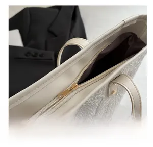 Detail shot of a smooth metal zipper and woven texture on a cream tote bag