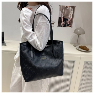 Detail of embossed floral patterns and golden logo plate on large black tote bag