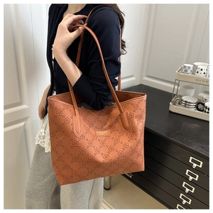 Detail of a brown tote bag featuring floral embossing and gold logo on the side