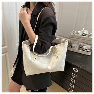 Detail of cream tote bag with floral embroidery and gold rivets on black blazer