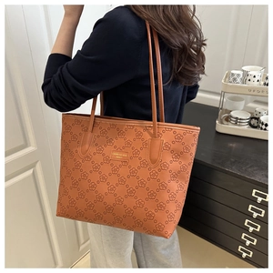 Close-up of brown tote bag featuring detailed floral embossing and golden brand plaque