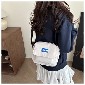 Detail of white canvas crossbody bag with blue brand patch shown on a female model