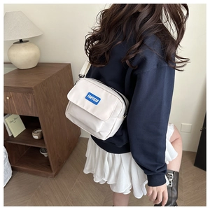 Detail view of the white canvas crossbody bag with blue logo patch worn by a model