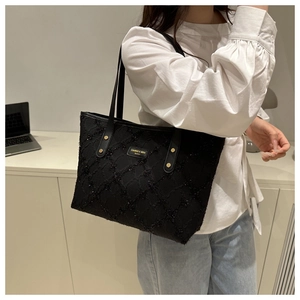 Detail of black quilted tote bag with gold studs and brand plate on textured fabric