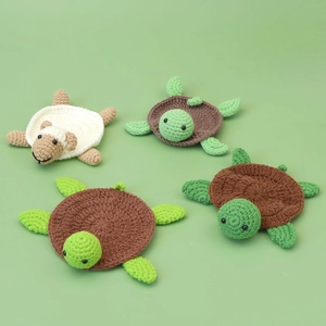Handmade crochet turtle and sheep coasters crafted with textured wool yarn on green background