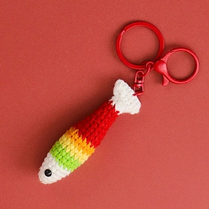 Macro detail of hand-crocheted rainbow fish keychain with vibrant yarn and red lobster clasp