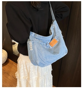 Detail of light blue denim tote with white letter embroidery and vintage orange leather tag