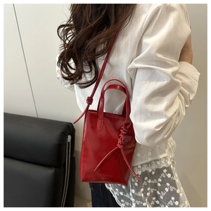 Detail view of red glossy leather vertical handbag with slim shoulder strap on a model
