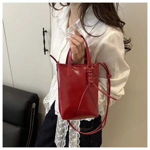 Detail of red glossy patent leather handbag with thin handles and shoulder strap
