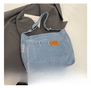 Detail of blue denim crossbody bag with multi-pockets, leather logo and frayed edges