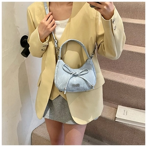 Détail du sac sous le bras bleu clair en forme de croissant avec nœud et logo en métal