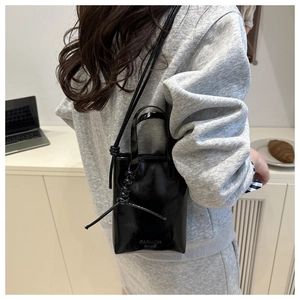 Detail of a minimalist black shiny mini handbag with a shoulder strap worn by a model