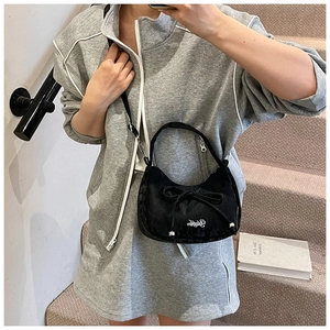 Détail du grand nœud papillon et du logo brodé blanc sur le sac à bandoulière noir