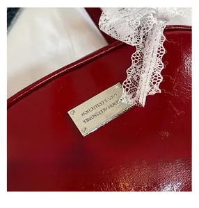 Close-up of red patent leather bag with silver metal tag and white lace bow detail