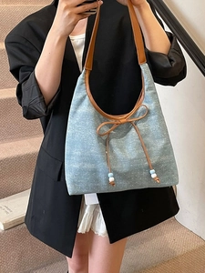 Light blue denim tote bag with leather bow and beads shown on shoulder of a model