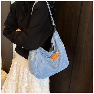 Macro shot of washed blue denim tote with distressed edges and vintage leather patch detail