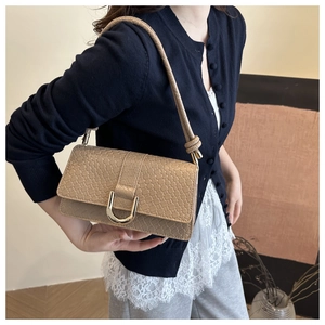 Detail of woven texture with gold U-shaped buckle on a khaki baguette shoulder bag